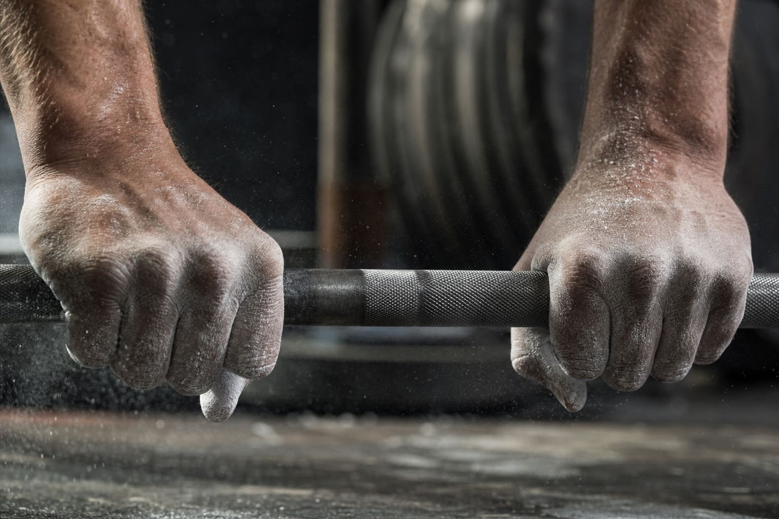 Chalked hands gripping a knurled barbell on a lifting platform.